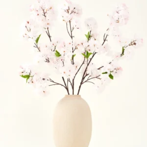 Der Seiden-Kunstblumenstrauß Cherry Blossom Blush 119 cm zeigt zarte, hellrosa Kirschblüten mit grünen Blättern in einer beigen Vase, ideal als künstliche Blumendekoration vor hellem Hintergrund.