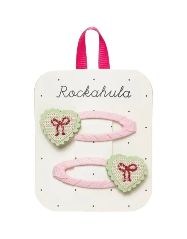 Sweet Heart Bow Haarspangen von Rockahula mit Herzmotiven, glitzernden roten Schleifen und rosafarbenen, stoffbezogenen Klickspangen.